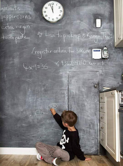 Copil desenand cu creta pe un perete cu vopsea blackboard.